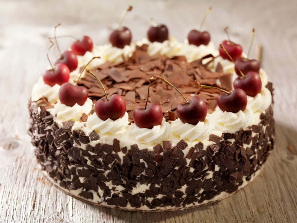 bolo redondo com lascas de chocolate em volta e no topo e cerejas