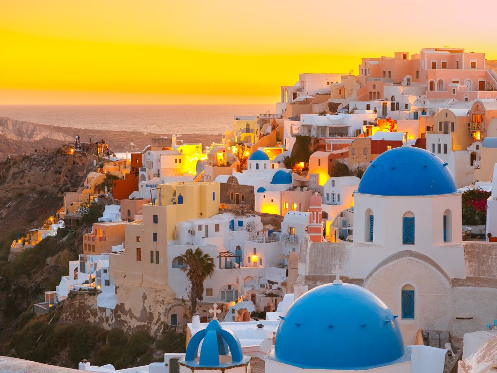 vista de santorini na grecia com construções em azul e no fundo o por do sol